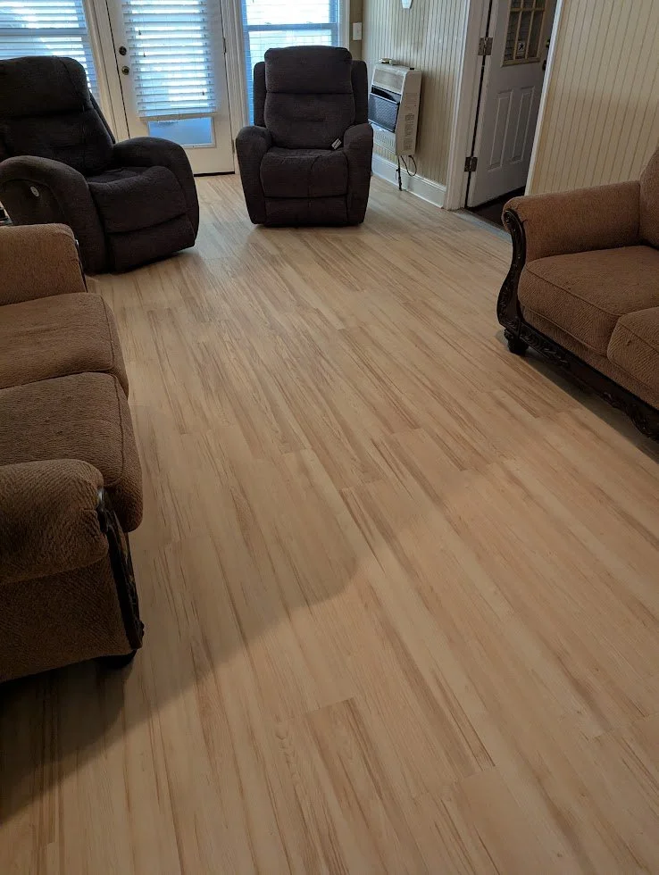 Living room with three armchairs and a sofa arranged around a hardwood floor. There is a door with glass panels, a window with blinds, and a wall heater.