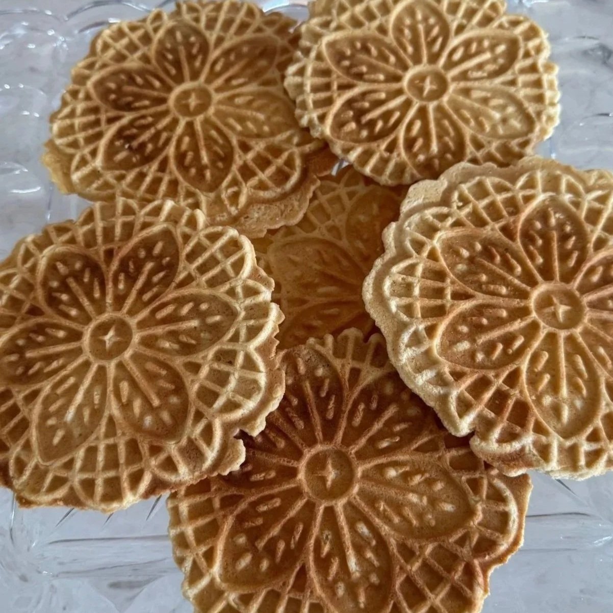 Close-up of decorative honeycomb-patterned waffle cookies arranged on a clear glass plate.
