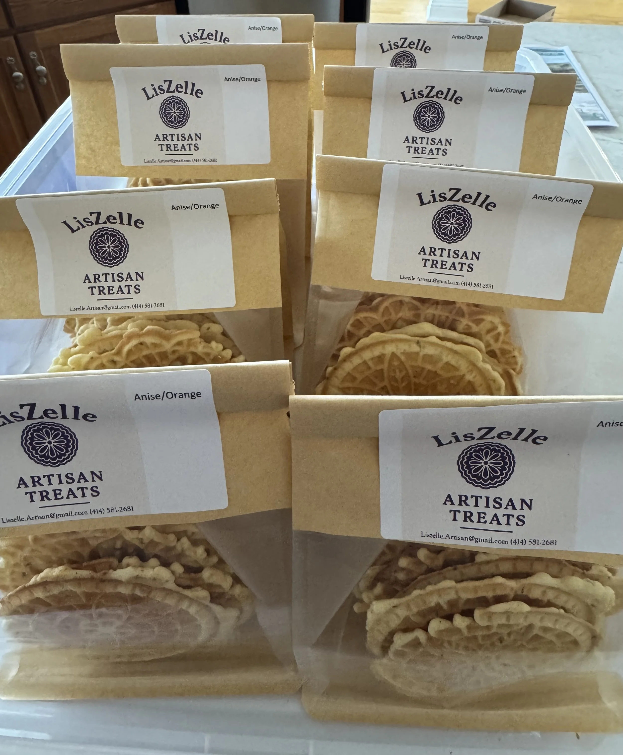 Several paper bags labeled 'LisZelle ARTISAN TREATS' with 'Anise/Orange' flavor, containing assorted homemade treats, displayed on a table.