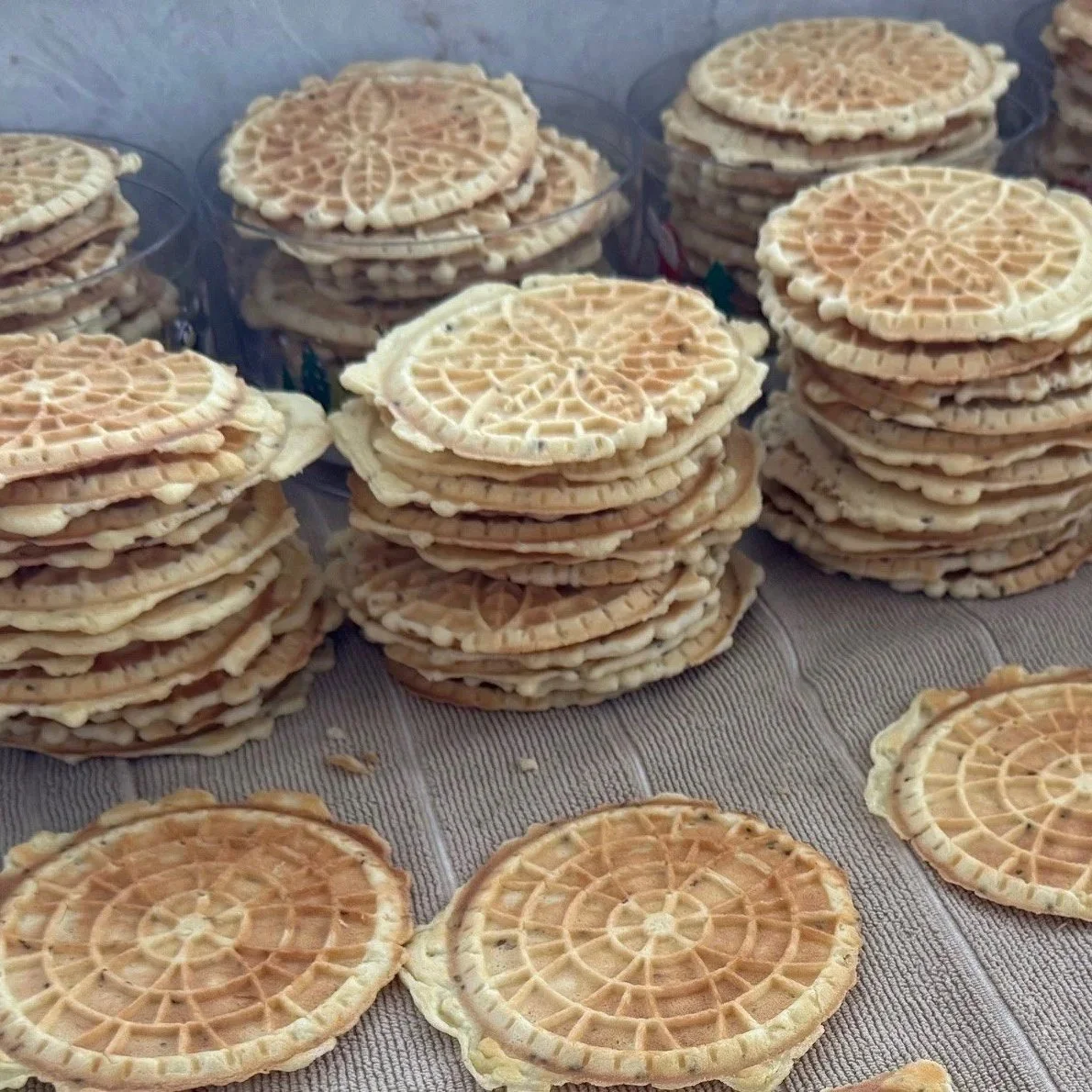 Stacks of waffle cookies with intricate spider-web patterns on top, arranged on a surface with some crispy cookies scattered around.