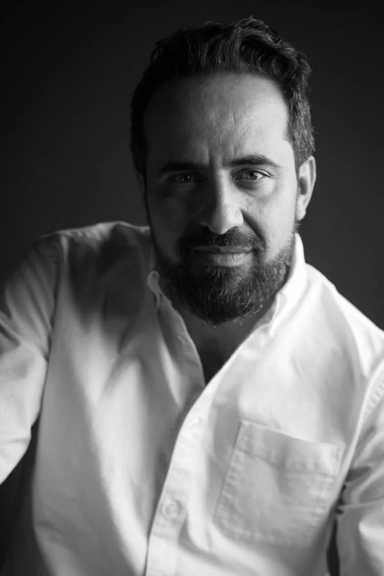 Retrato en blanco y negro de un hombre con barba, cabello oscuro y camisa blanca, sonriendo ligeramente, mirada directa a la cámara.