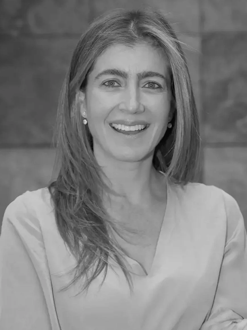 Retrato en blanco y negro de una mujer con cabello largo, sonrisa, usando una blusa clara y pendientes, fondo de madera.