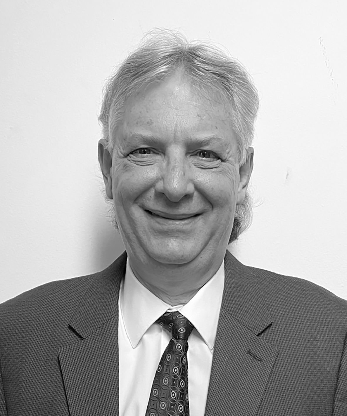 Retrato en blanco y negro de un hombre con cabello gris, sonriendo, con traje y corbata