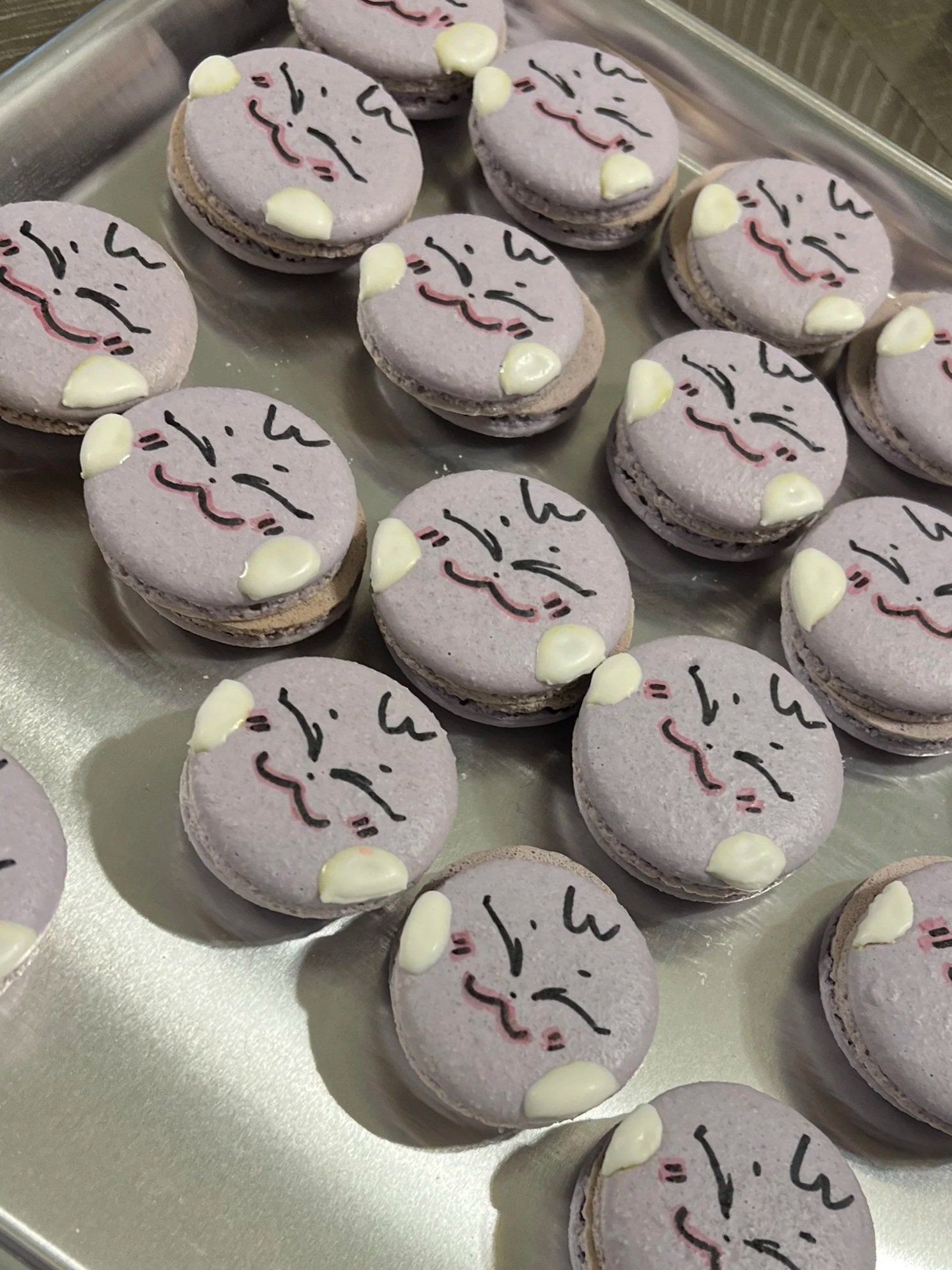 A tray of purple macarons decorated with smiley face drawings and small white dots.