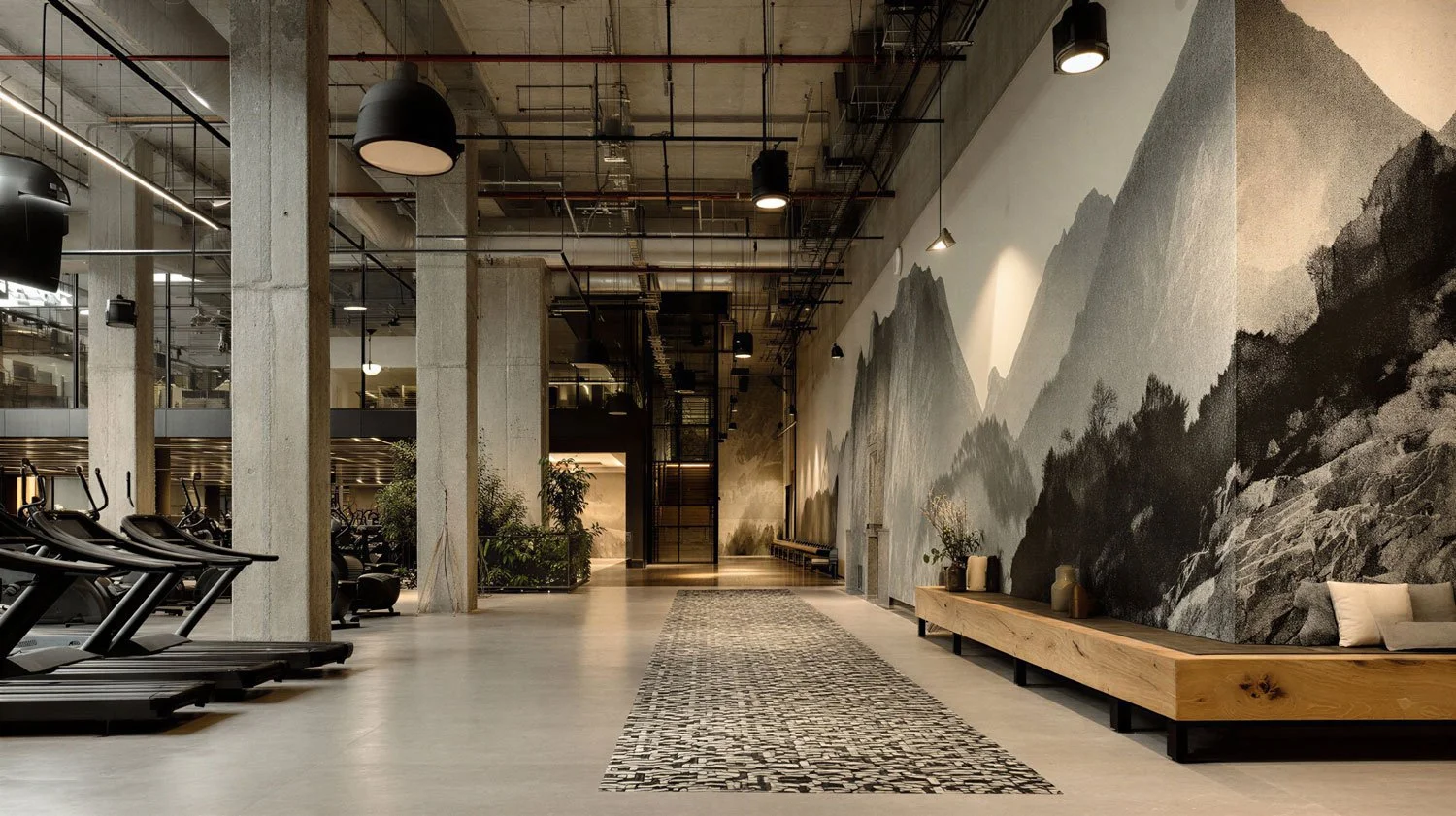 Innenraum eines Fitnessstudios mit Laufbändern, einem Wandbild mit Bergmotiven und einer Sitzbank mit Dekorationen.