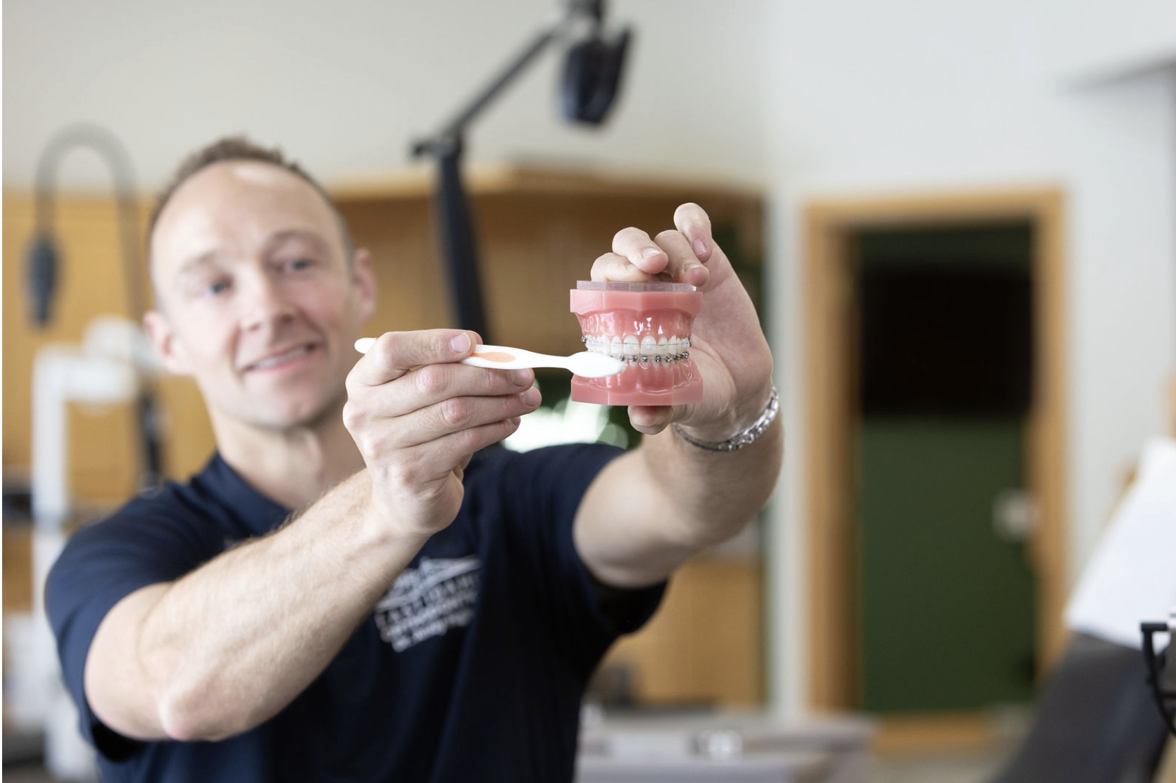 A man holding dental model with pink gums and white teeth, brushing the model's teeth with a toothbrush.