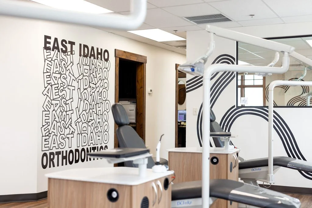 Orthodontic office with dental chairs, wall art displaying 'East Idaho Orthodontics', and black and white curved line designs on the walls.