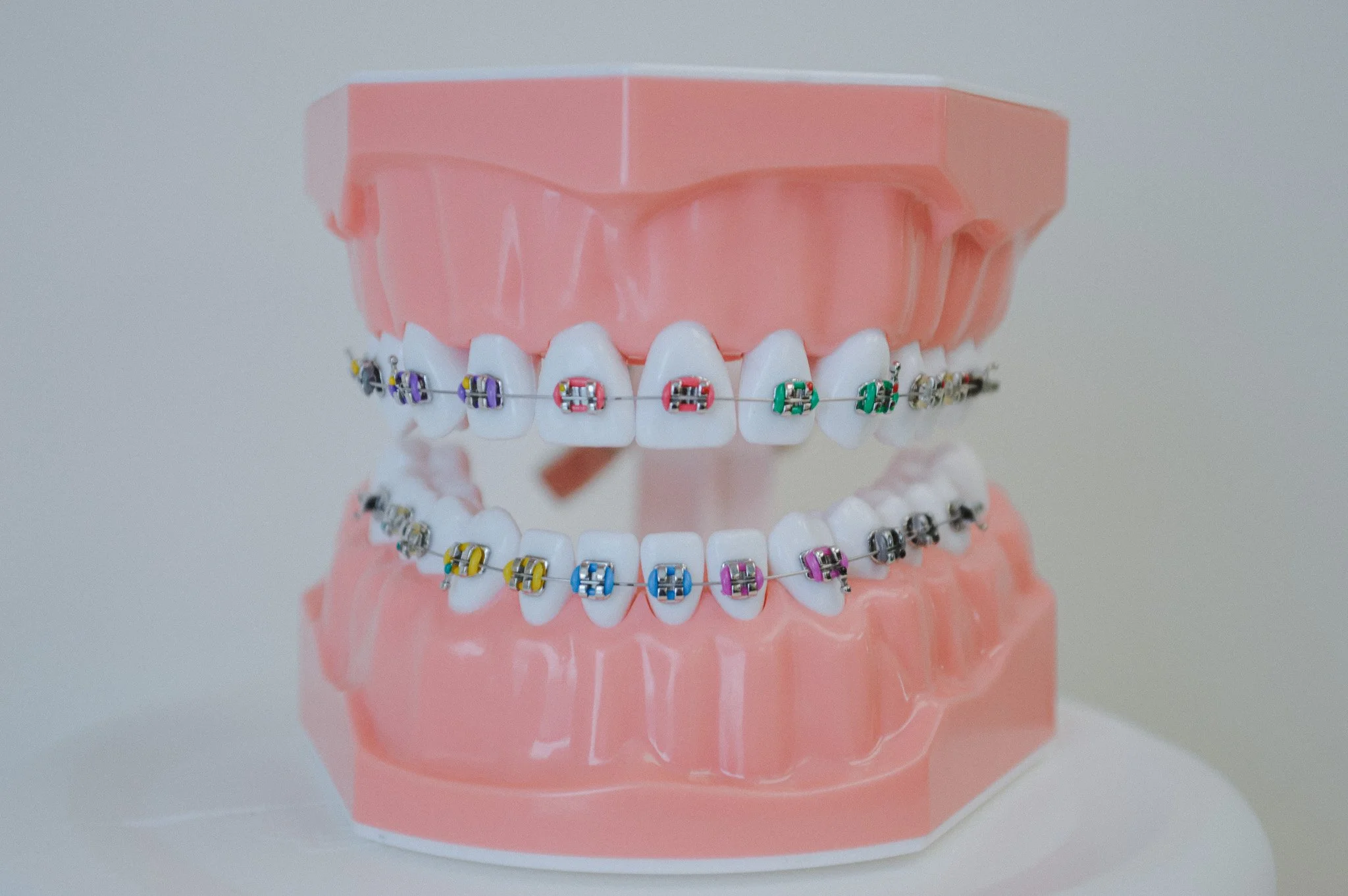 A dental model of teeth with colorful orthodontic braces on both the top and bottom rows.
