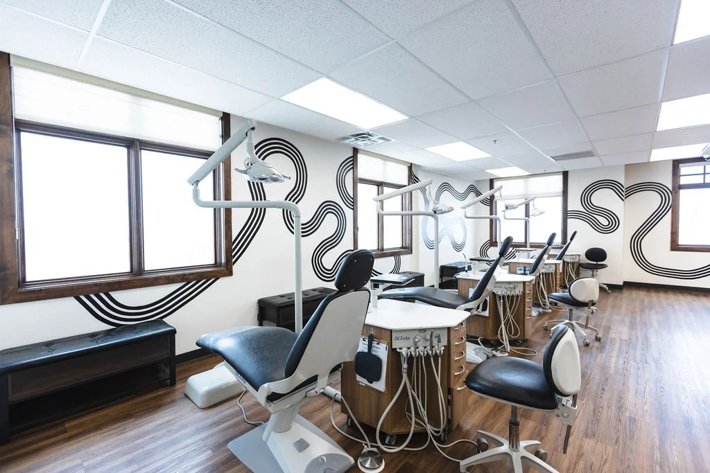 Dental treatment chairs and equipment in a clinic room with large windows and modern decor.