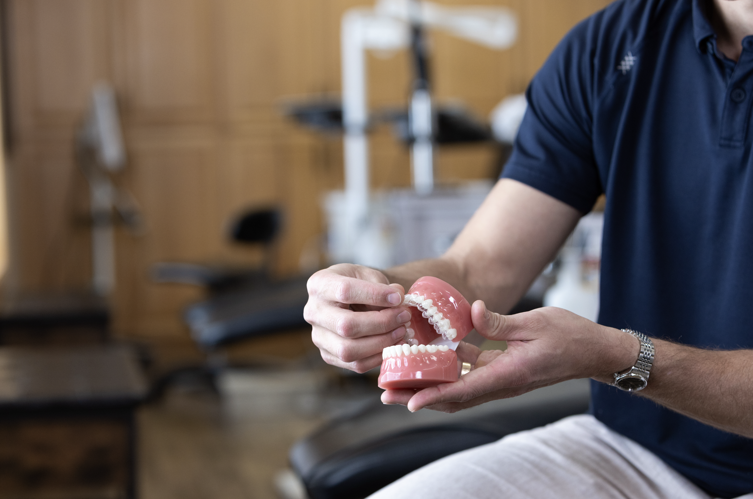 A person holding a dental model showing teeth, with a dental clinic or office in the background.