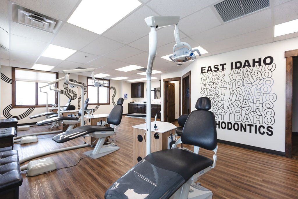 A dental clinic with dental chairs, overhead lights, and dental equipment, featuring a wall with the text 'East Idaho Orthodontics'.