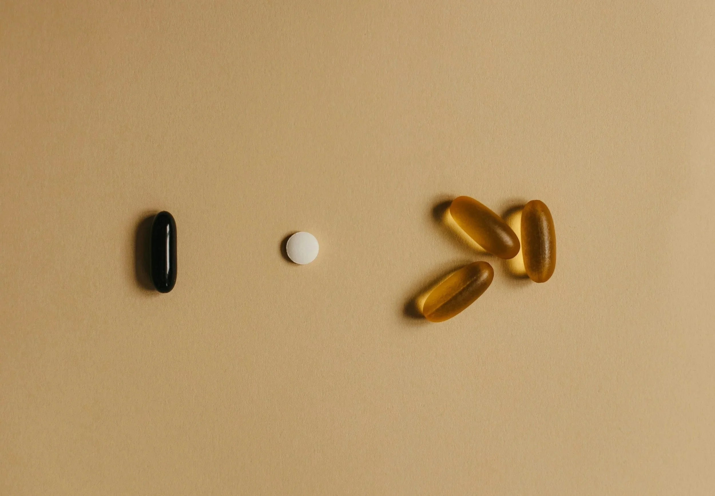 An arrangement of pills and tablets resembling a human face, with three brown capsules at the top, a white pill in the center, and a black capsule at the bottom.