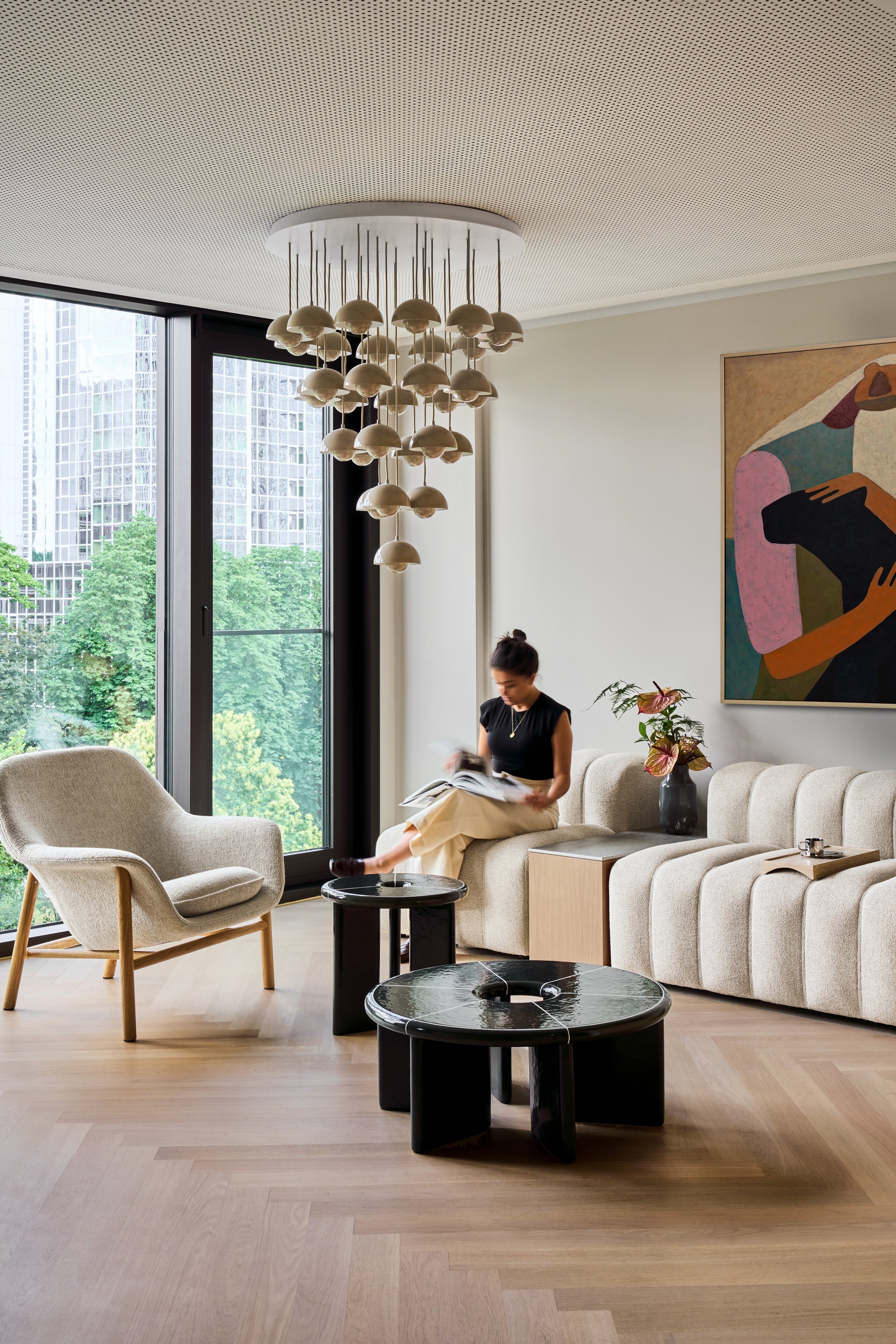 Modernes Wohnzimmer mit beigem Sofa, Holzsessel und schwarzem Couchtisch – Innenarchitektur mit abstraktem Wandbild und Design-Hängeleuchte