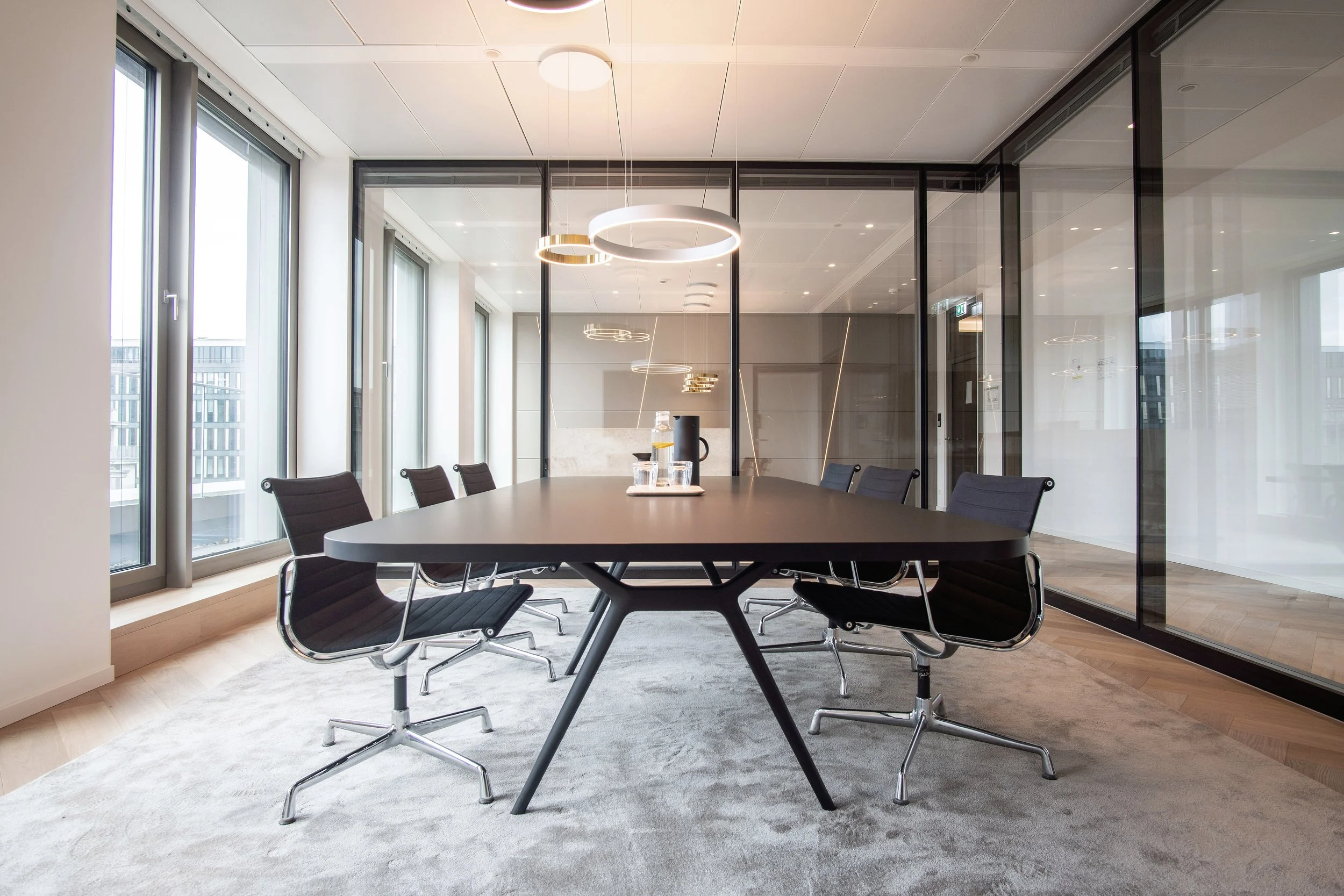 Konferenzraum mit ovalem Tisch, Glaswänden und Design-Hängeleuchte – Innenarchitektur für Büroräume