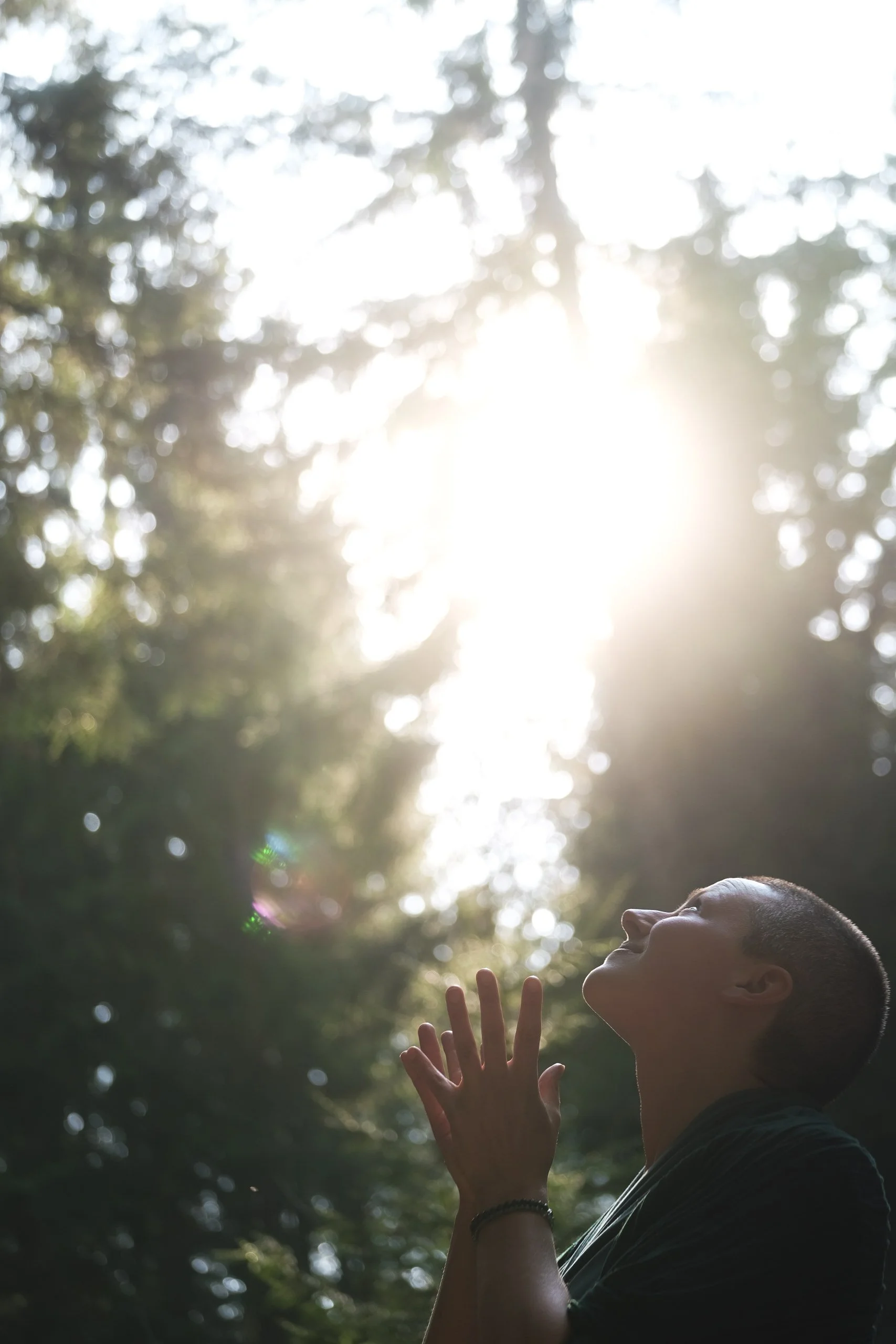 Eine Frau steht im Freien und sieht nach oben, während die Sonne durch die Bäume scheint.