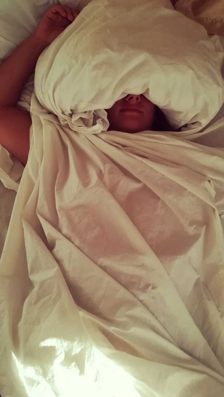 Person liegt unter einer dicken, weißen Bettdecke im Bett.