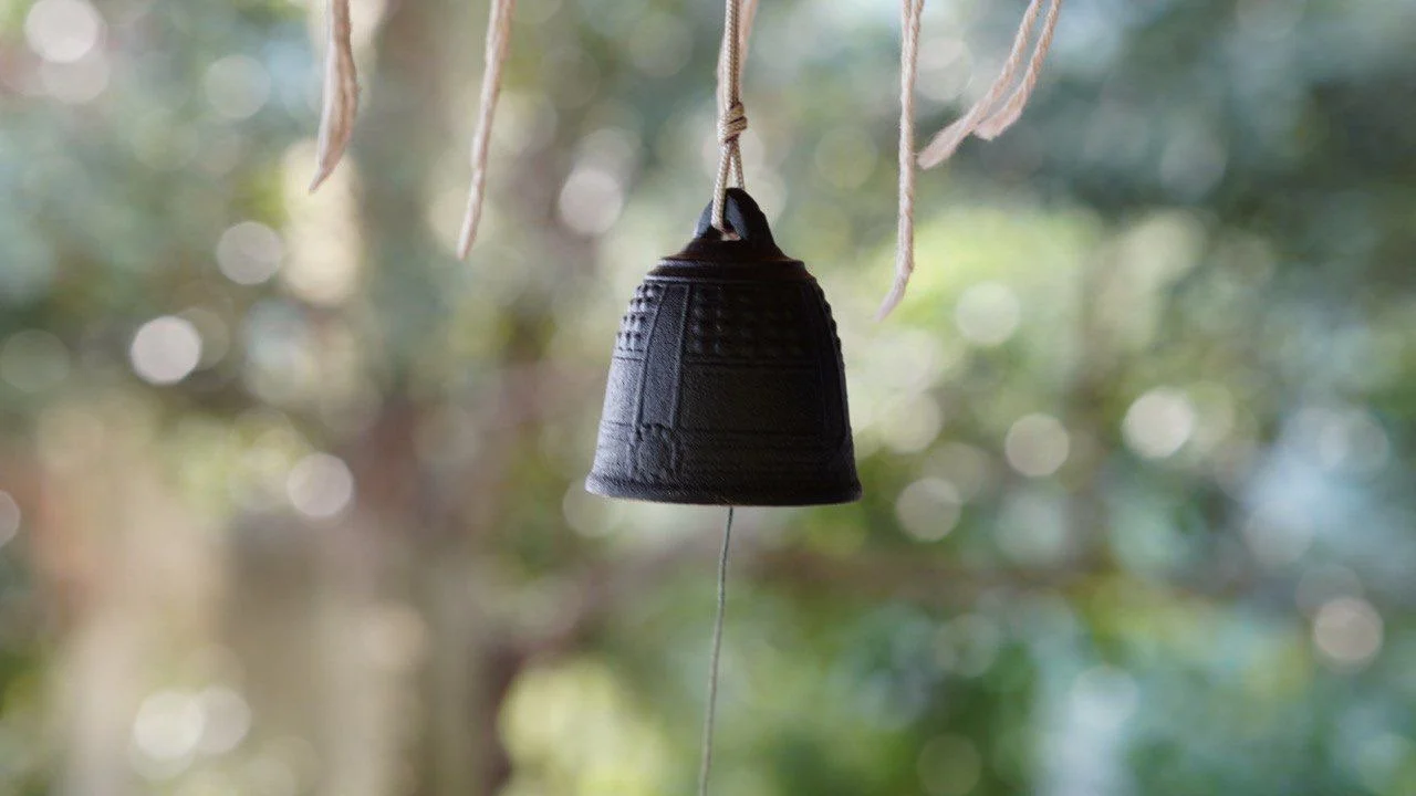 Ein schwarzes kleine Glocke hängt an einem Seil vor einem unscharfen natürlichen Hintergrund.