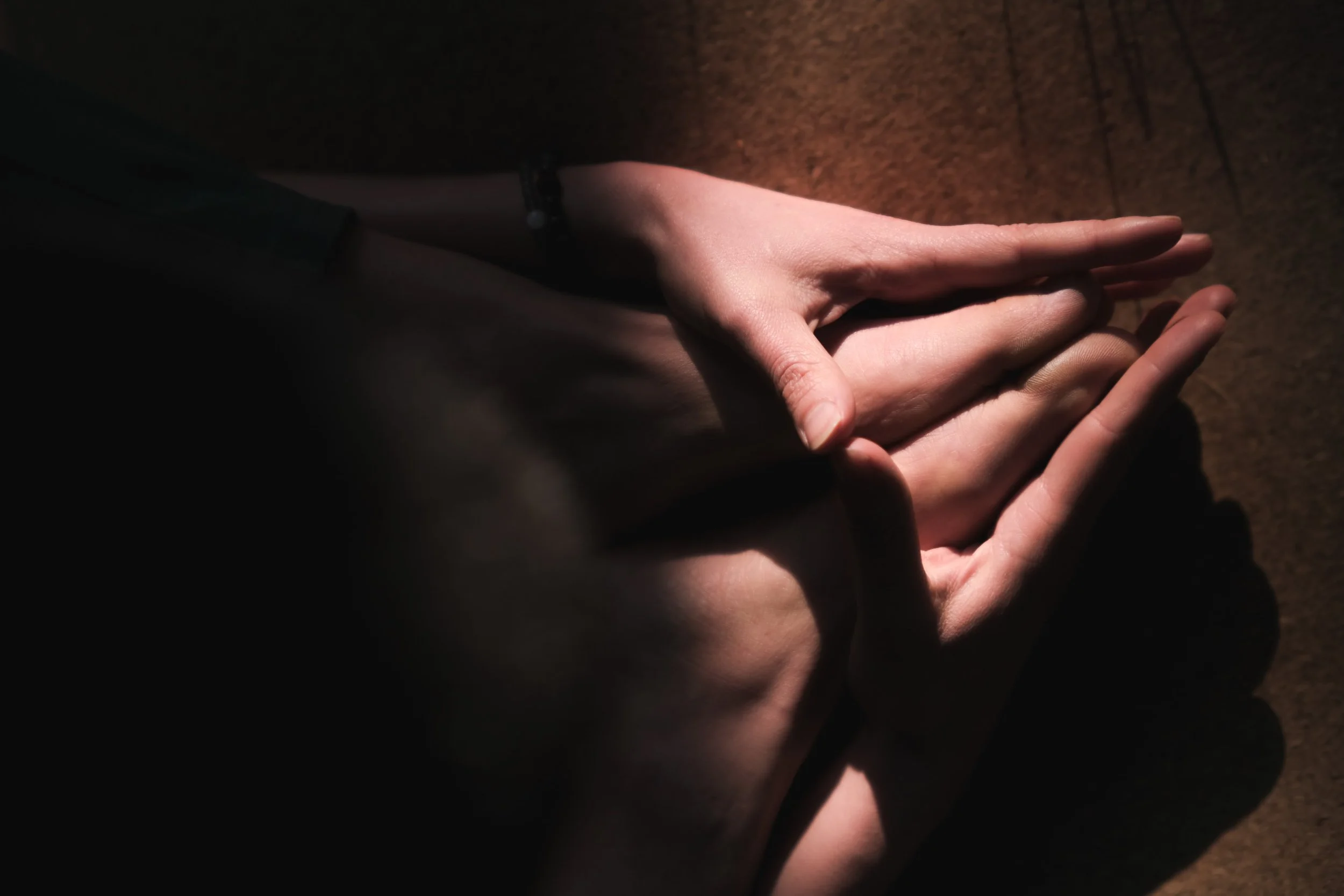 Close-up of a person's hands resting on a wooden surface, illuminated by a dim, warm light.