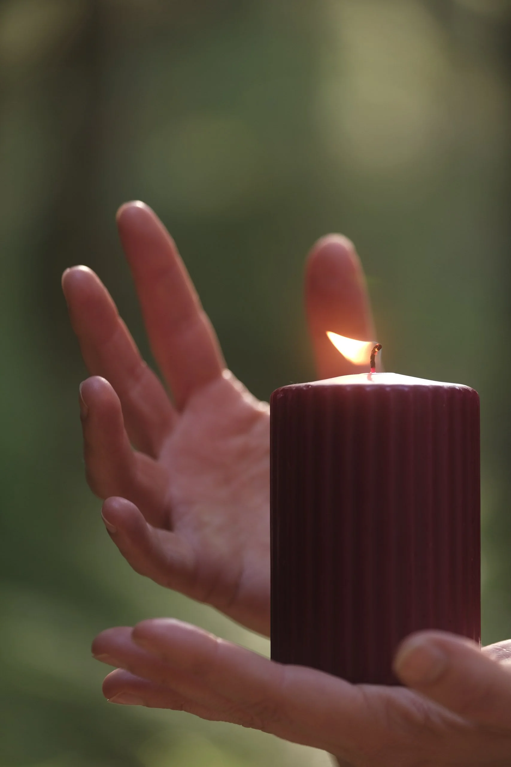 Eine Hand hält eine brennender Kerze und schützt deren Flamme