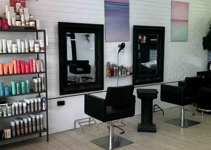 Hair salon with black styling chairs, mirrors, and shelves of hair products on a white brick wall.