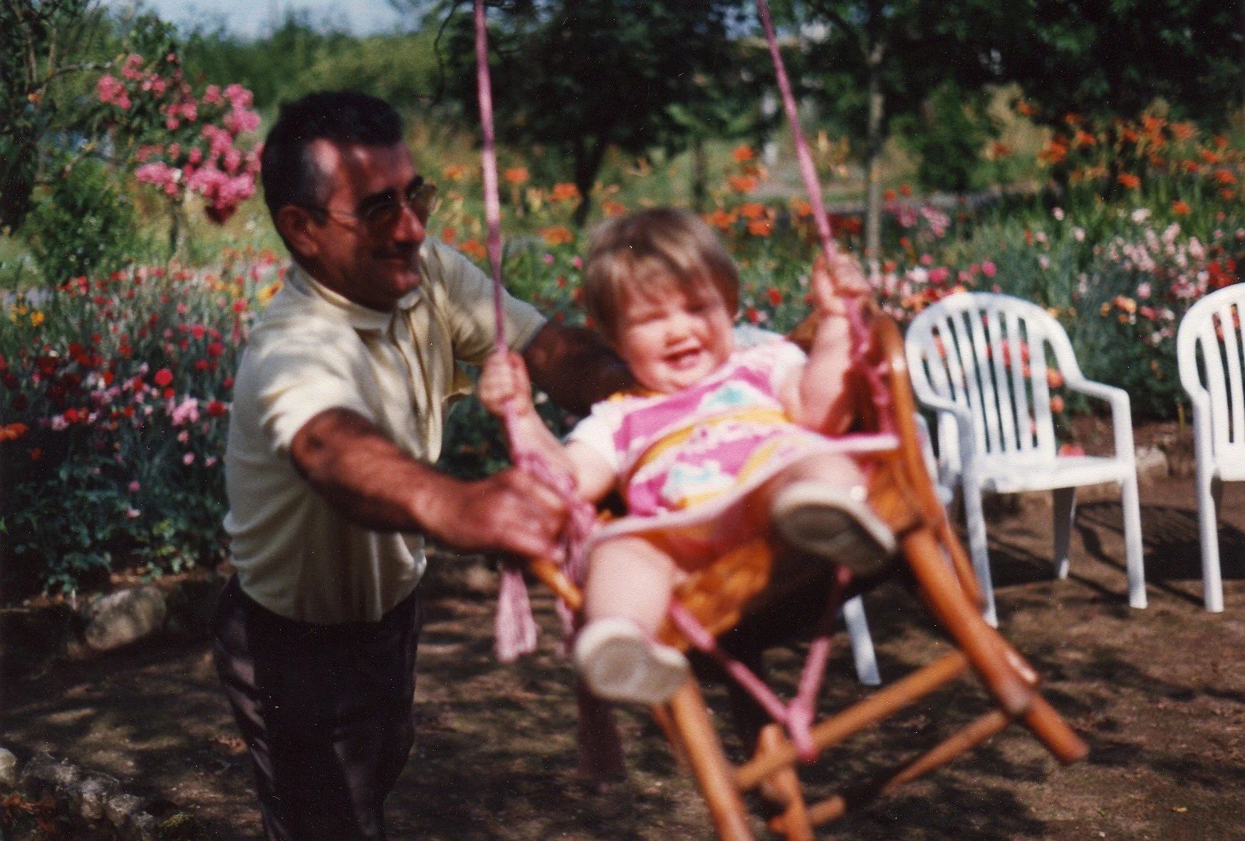Homme poussant une petite fille souriante sur une balançoire dans un jardin fleuri — photographie pour la campagne de communication Pana po'o par Deux lignes Studio