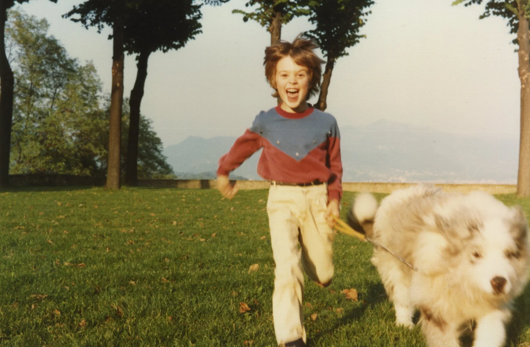Garçon courant dans un parc en jouant avec un chien blanc et noir, avec montagnes en arrière-plan — photographie campagne Pana po'o par Deux lignes Studio