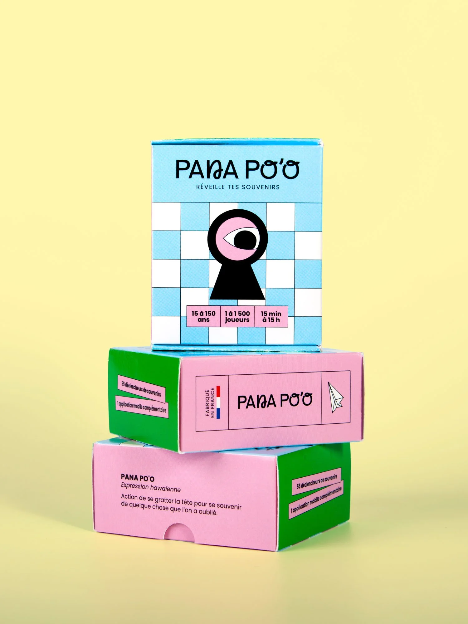 Boîtes de jeu de cartes Pana po'o colorées empilées sur fond jaune, dont une bleue marquée ‘Pana po'o et une rose avec texte descriptif — packaging par Deux lignes Studio