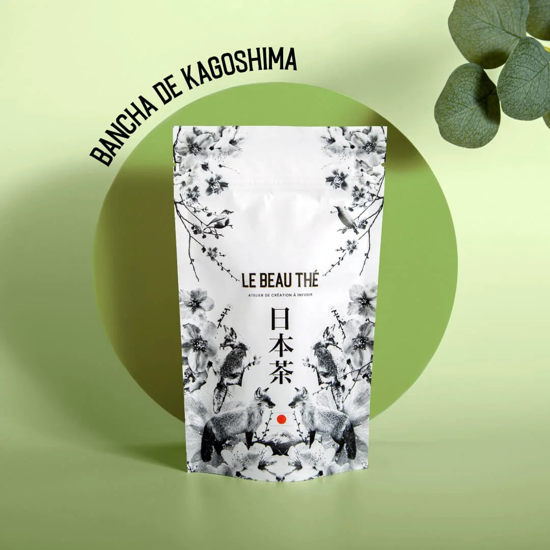Packaging de thé japonais noir et blanc avec illustrations florales et animales, posé sur fond vert — création graphique Le Beau Thé par Deux lignes Studio