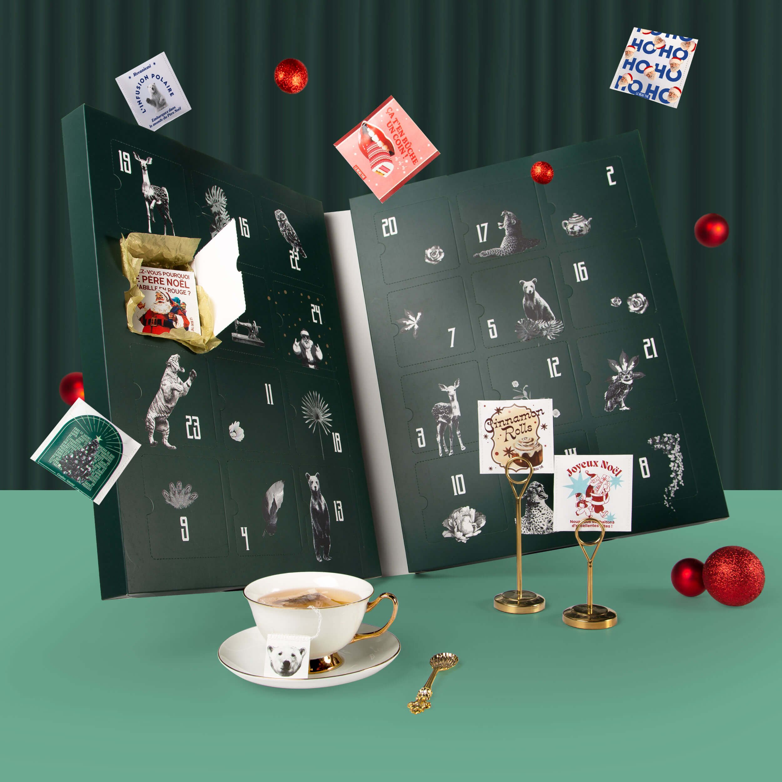 Coffret calendrier de l'avent vert illustré d'animaux et d'étoiles avec 24 cases numérotées, entouré de décorations de Noël vertes — packaging Le Beau Thé par Deux lignes Studio