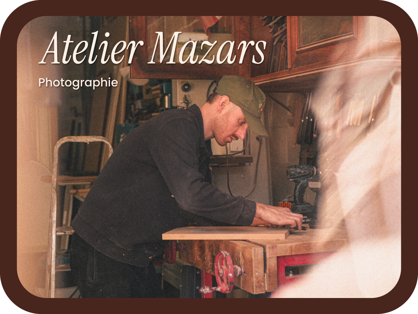 A man working in a woodworking shop, using a cordless drill on a piece of wood at a workbench, surrounded by woodworking tools and equipment.