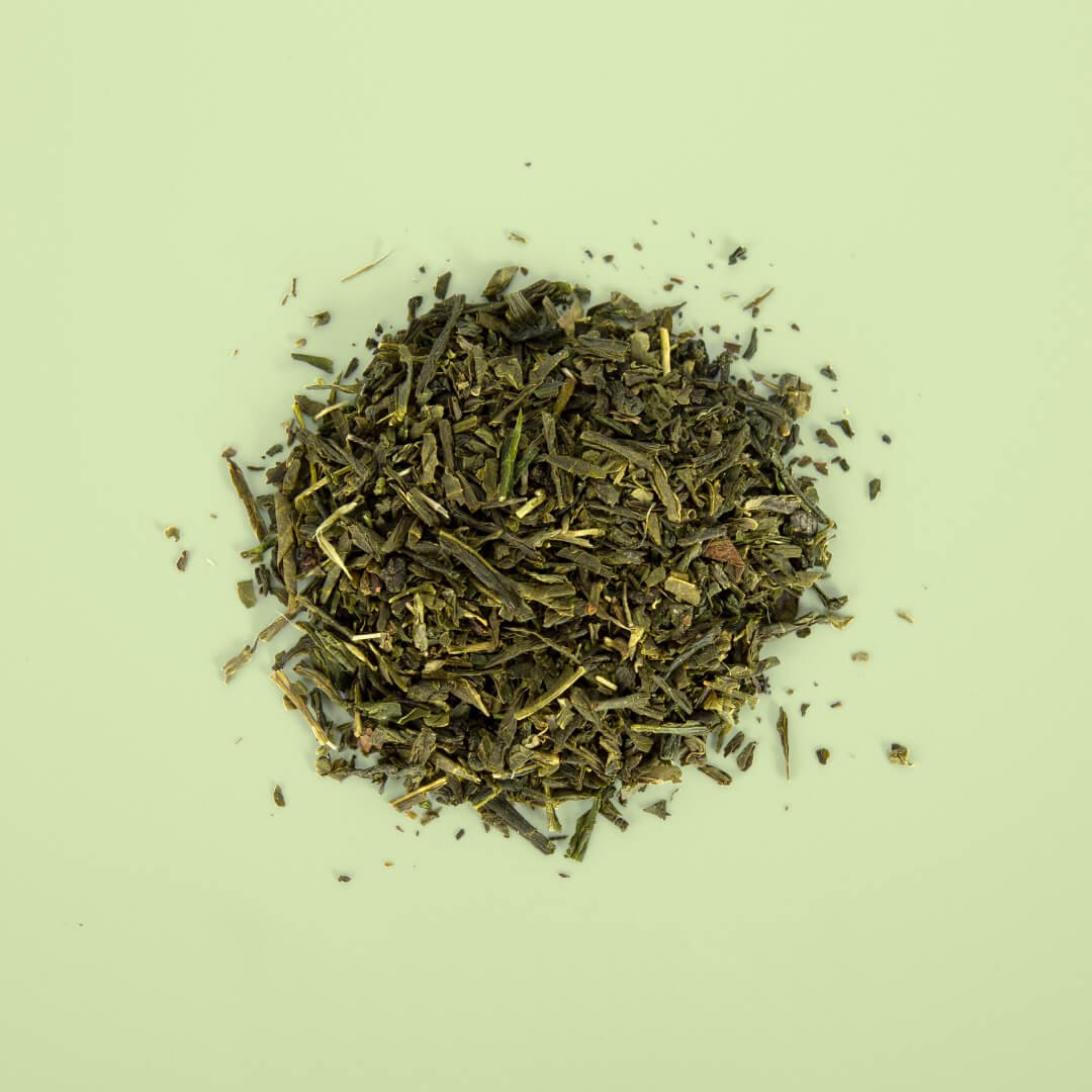Feuilles de thé vert vrac mélangées à de la poudre de yuzu séché sur fond vert clair — shooting produit Le Beau Thé par Deux lignes Studio
