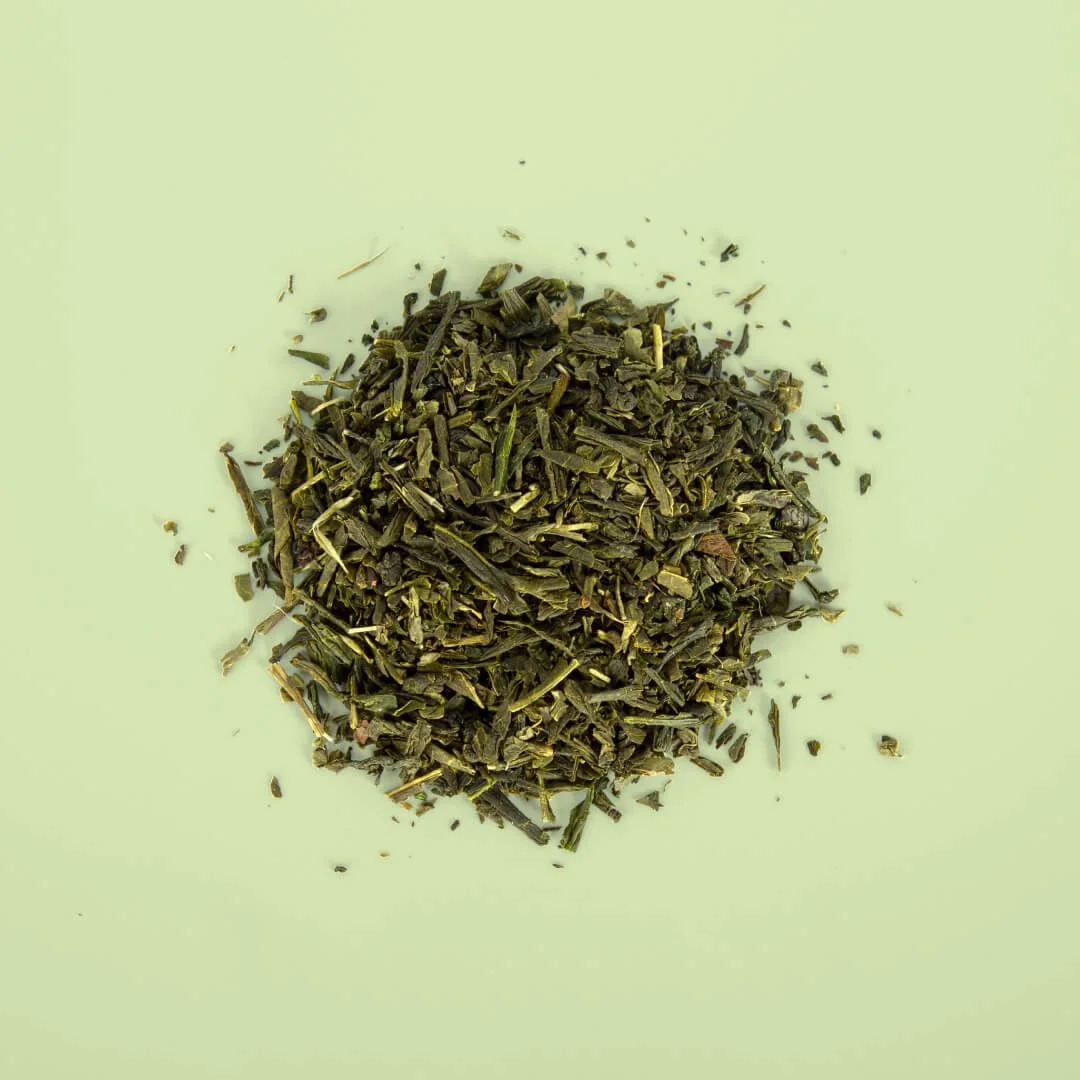 Dried green tea leaves scattered on a light green surface.