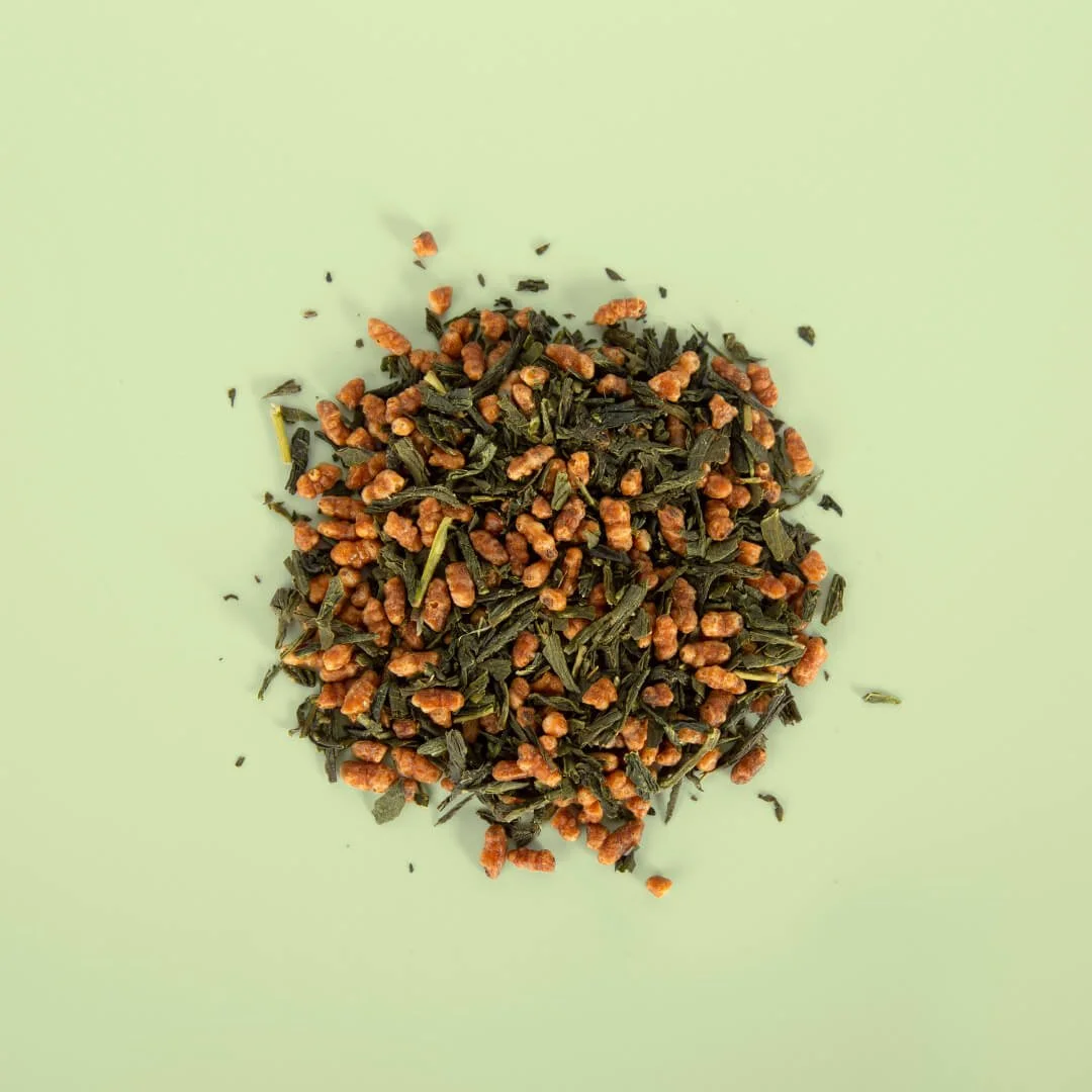 A pile of loose leaf green tea mixed with dried yuza tea powder on a light green background.