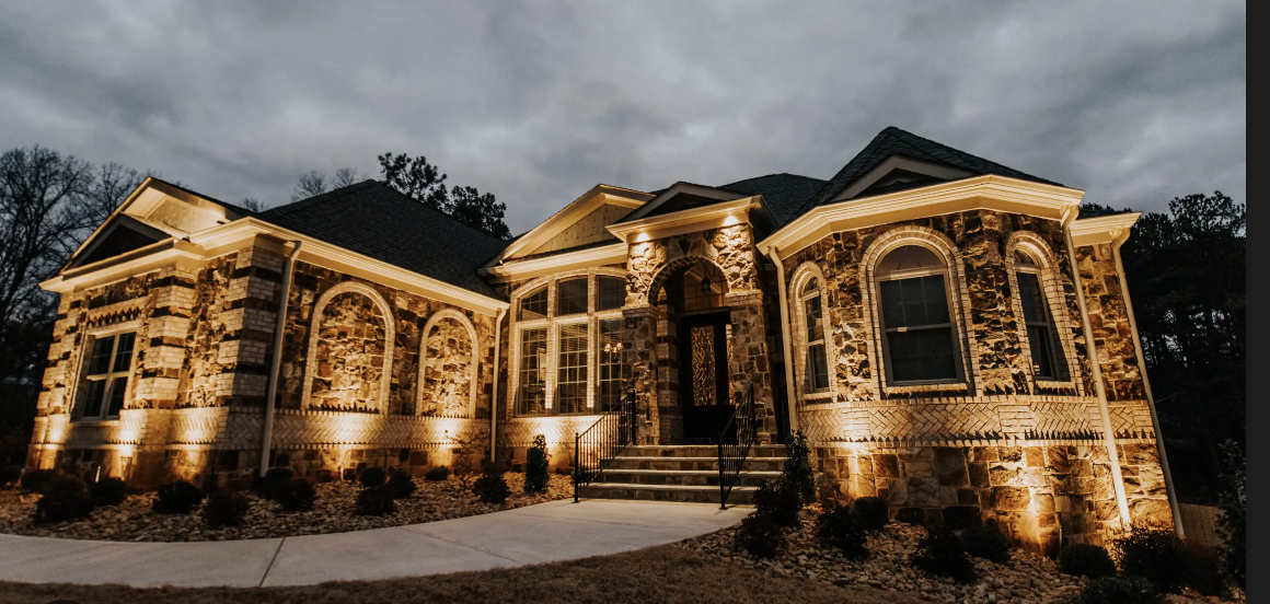 Illuminated large stone house exterior at dusk with arched windows and a staircase leading to the front door.