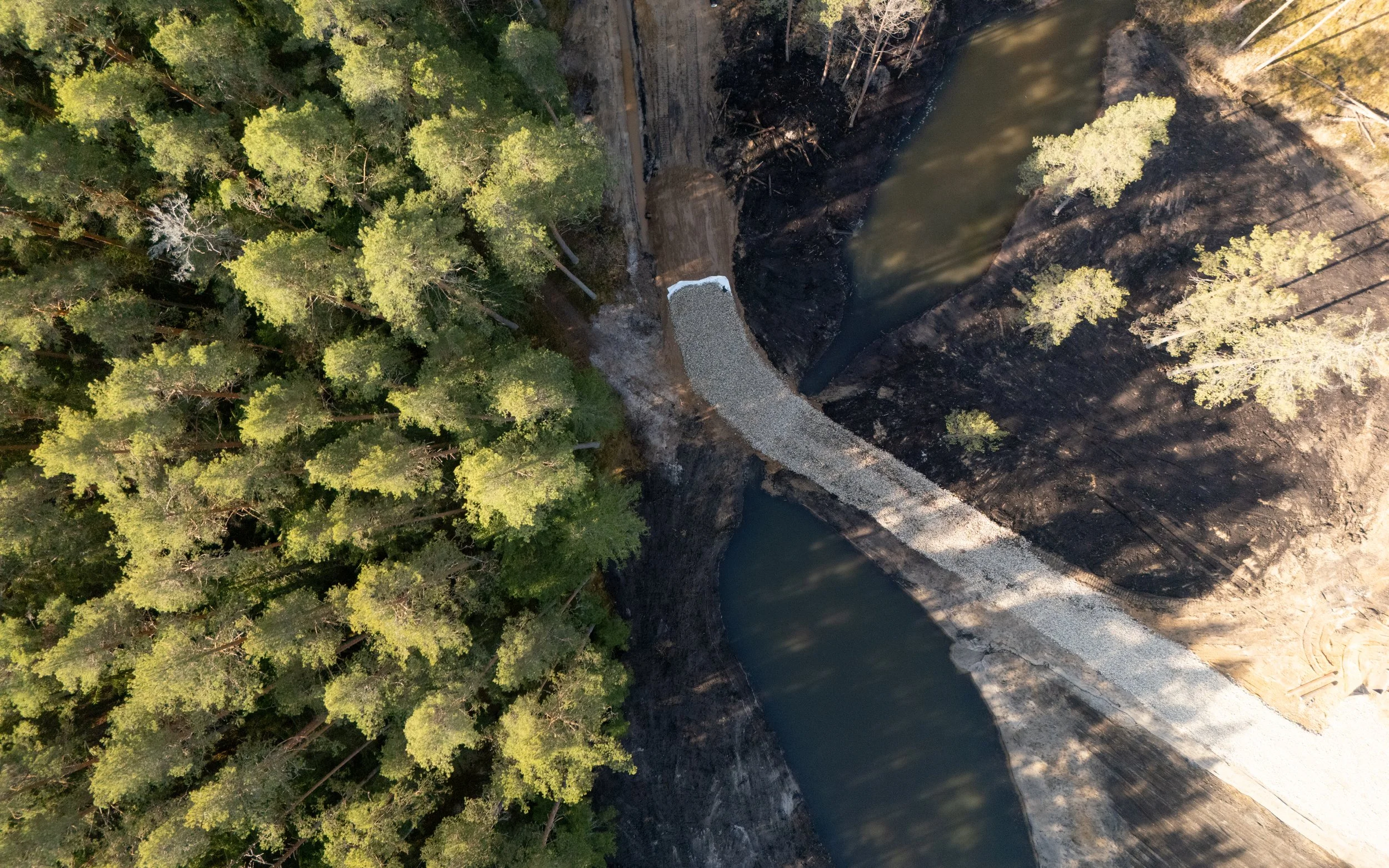 An aerial view of a dam with water flowing through, surrounded by dense green forest on one side and a rocky area on the other.