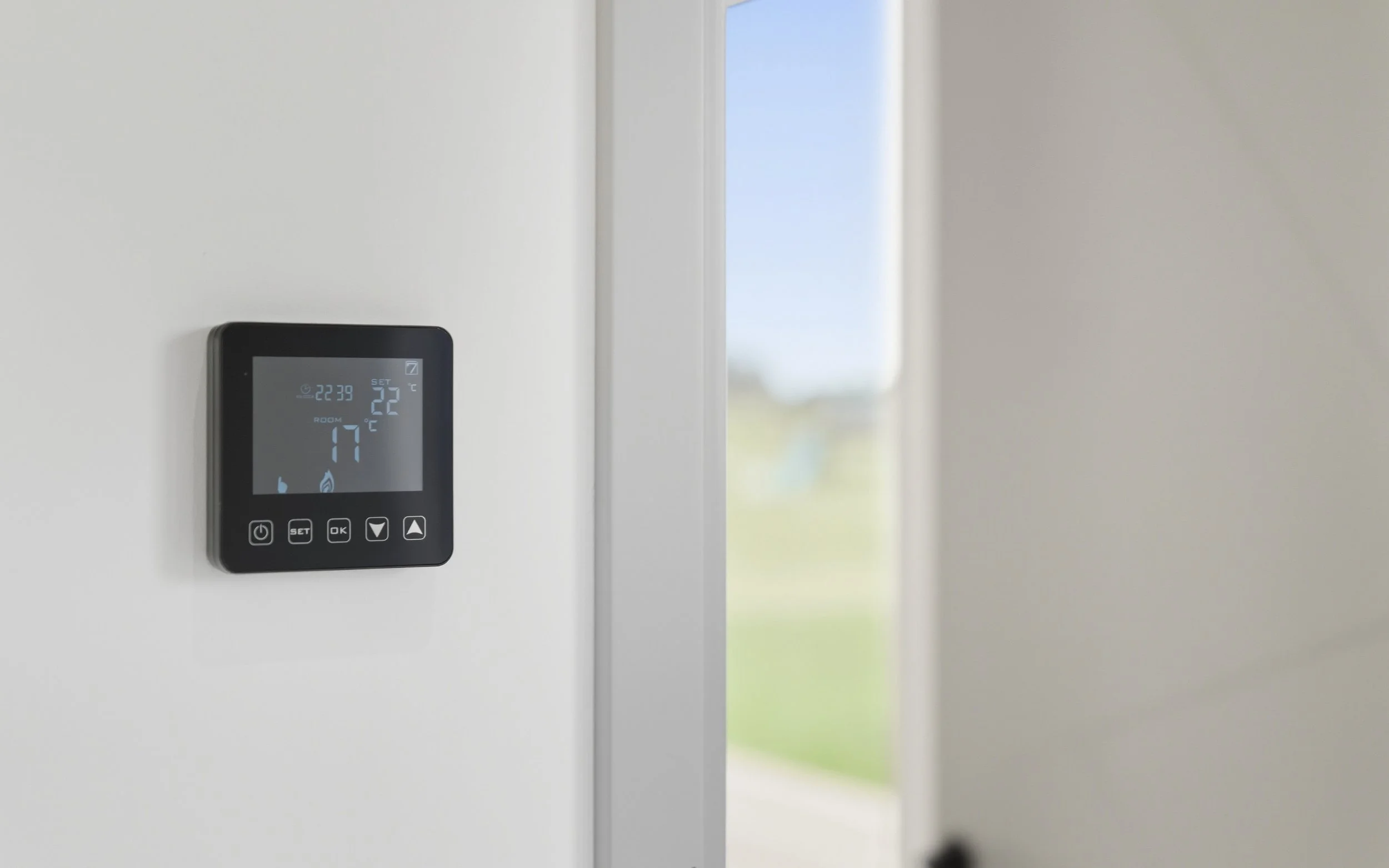 A digital thermostat on a white wall shows the current time as 22:39 and the room temperature as 17°C, with a setting of 22°C. There is a window in the background with a blurred outdoor view.