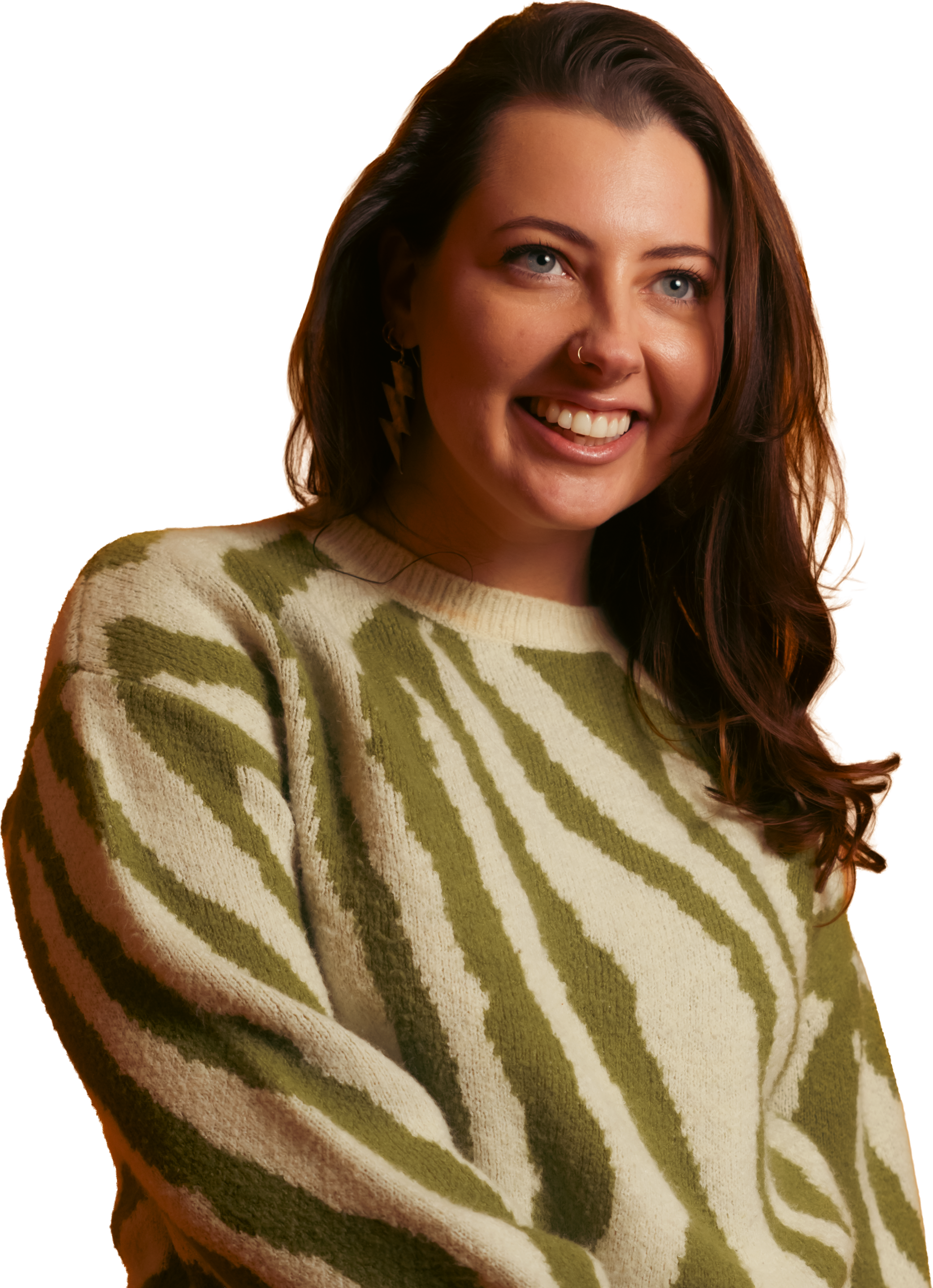 A young woman with long brown hair, blue eyes, and a nose ring smiling, wearing a cream-colored sweater with green zebra-like stripes and lightning bolt earrings.