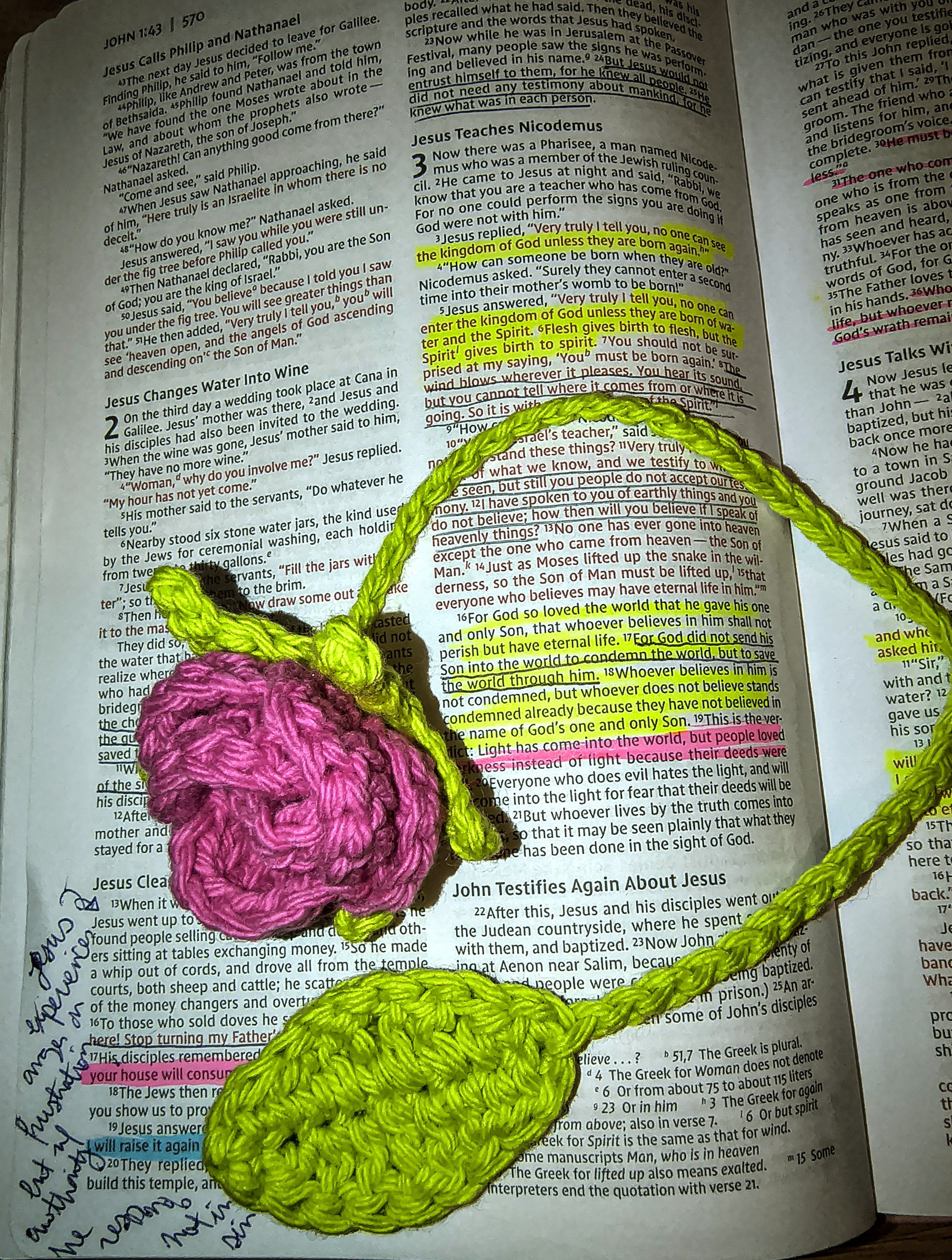 The image shows a sheet of paper with Bible verses and highlighted text, overlaid with a colorful handmade crochet item. There is a pink and green crochet rose bookmark.