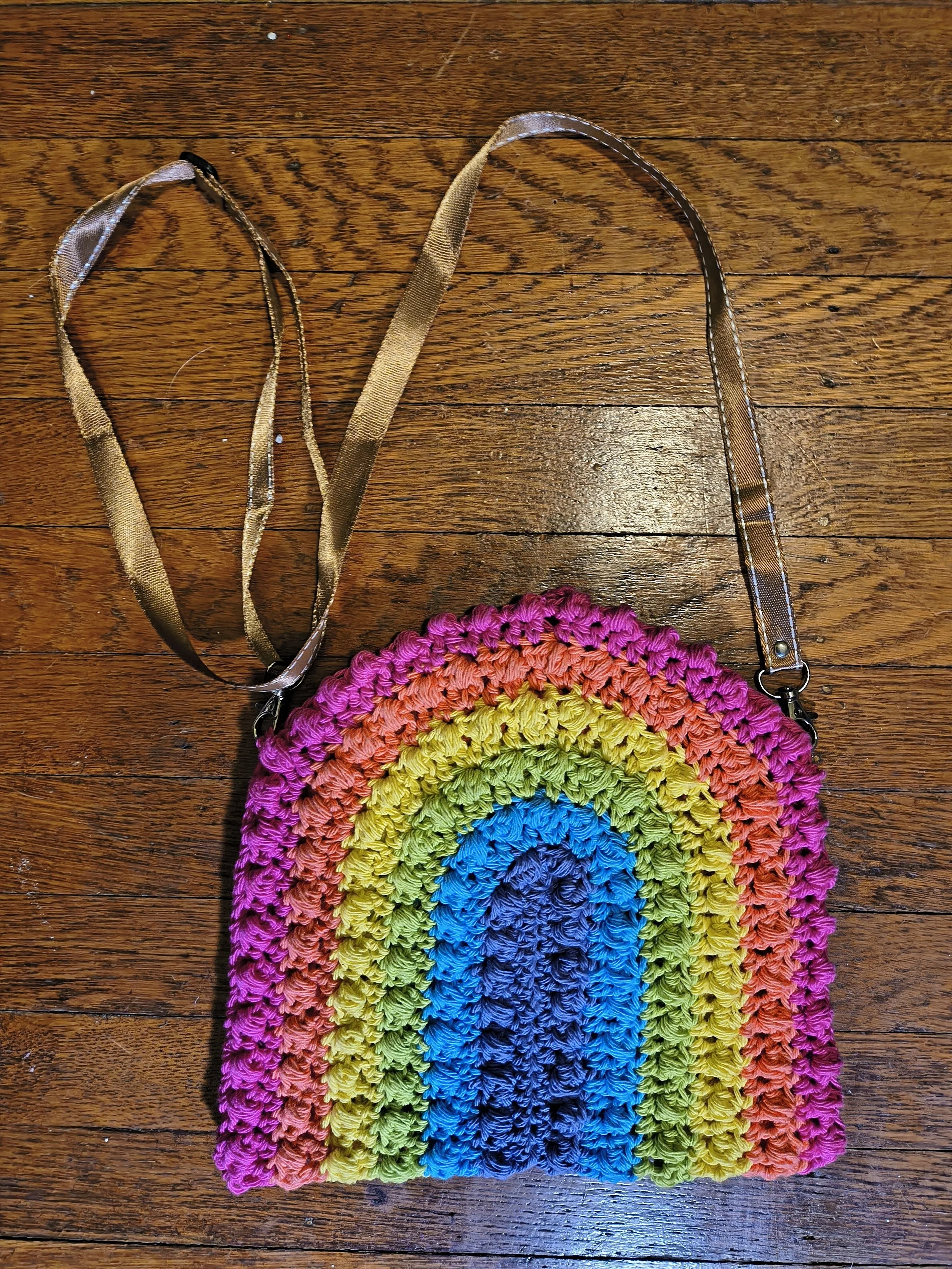 Colorful woven rainbow-shaped bag with pink, orange, yellow, green, blue, and purple stripes on a wooden surface.