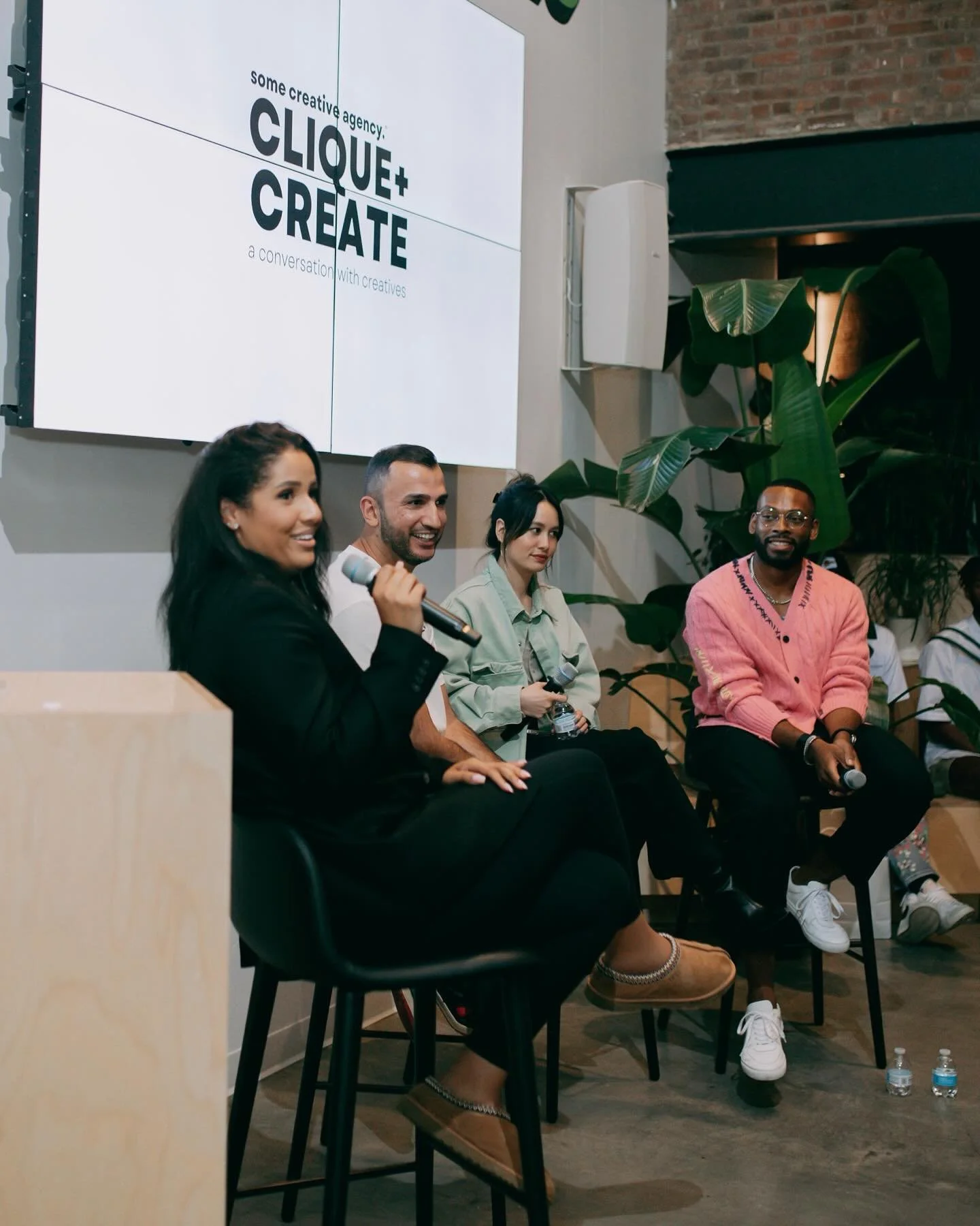 A diverse group of four people sitting on a stage panel, three women and Brandon Smithwrick, holding microphones during a discussion event.