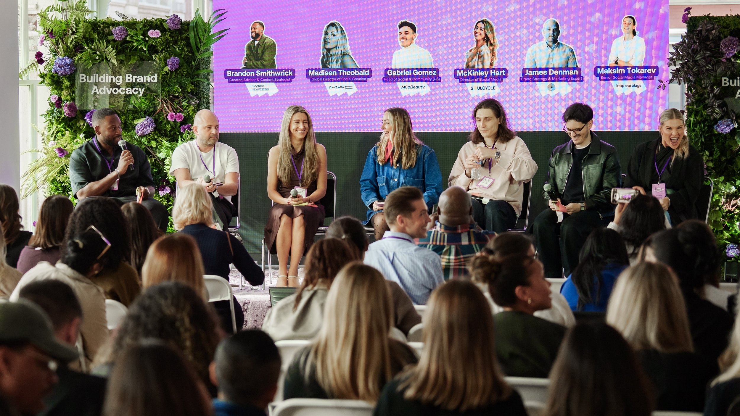 A panel discussion at a conference about building brand advocacy, featuring six diverse speakers seated on a stage in front of an audience. 