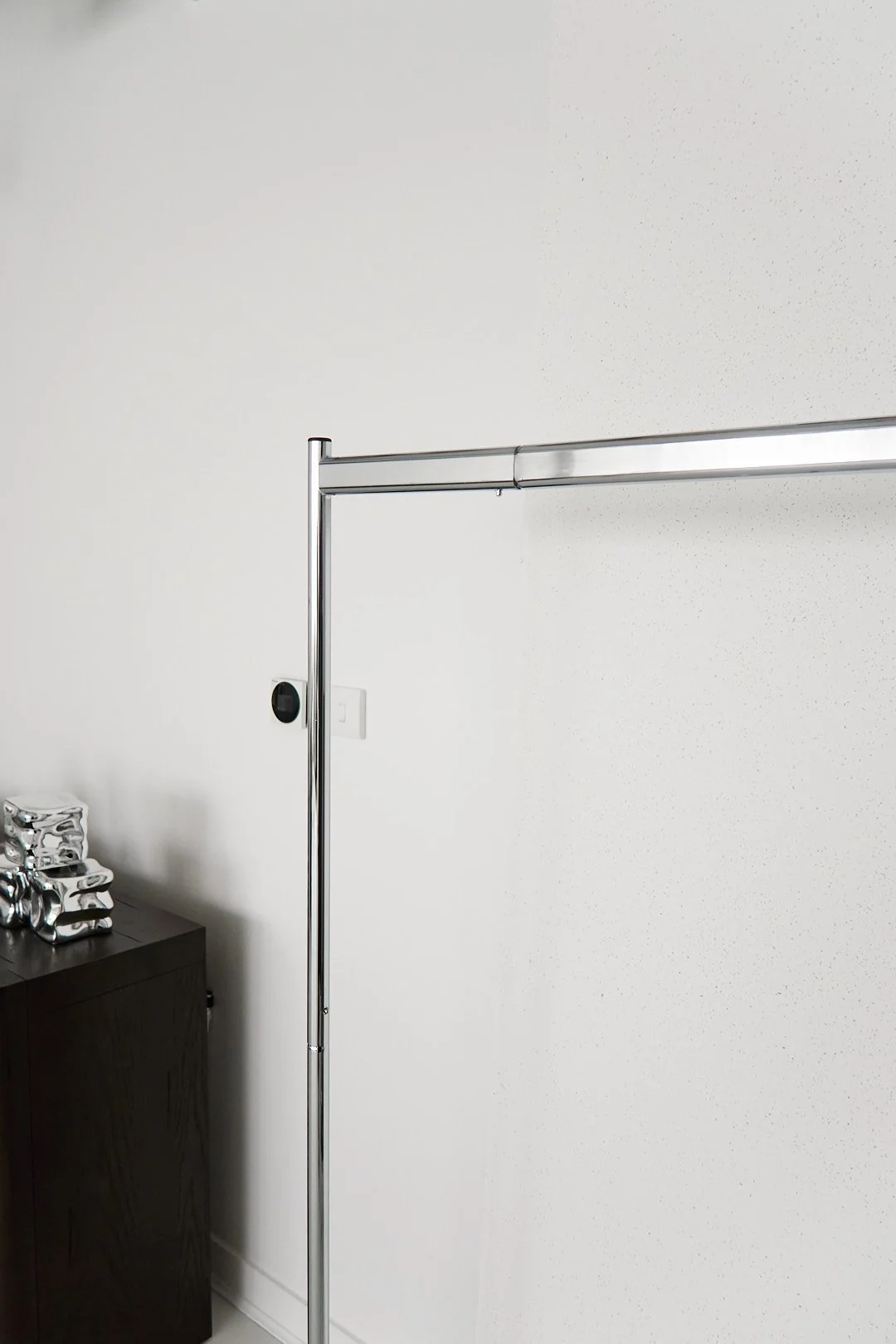 Empty room with a metal clothing rack and a black cabinet with some decorative silver objects on top.