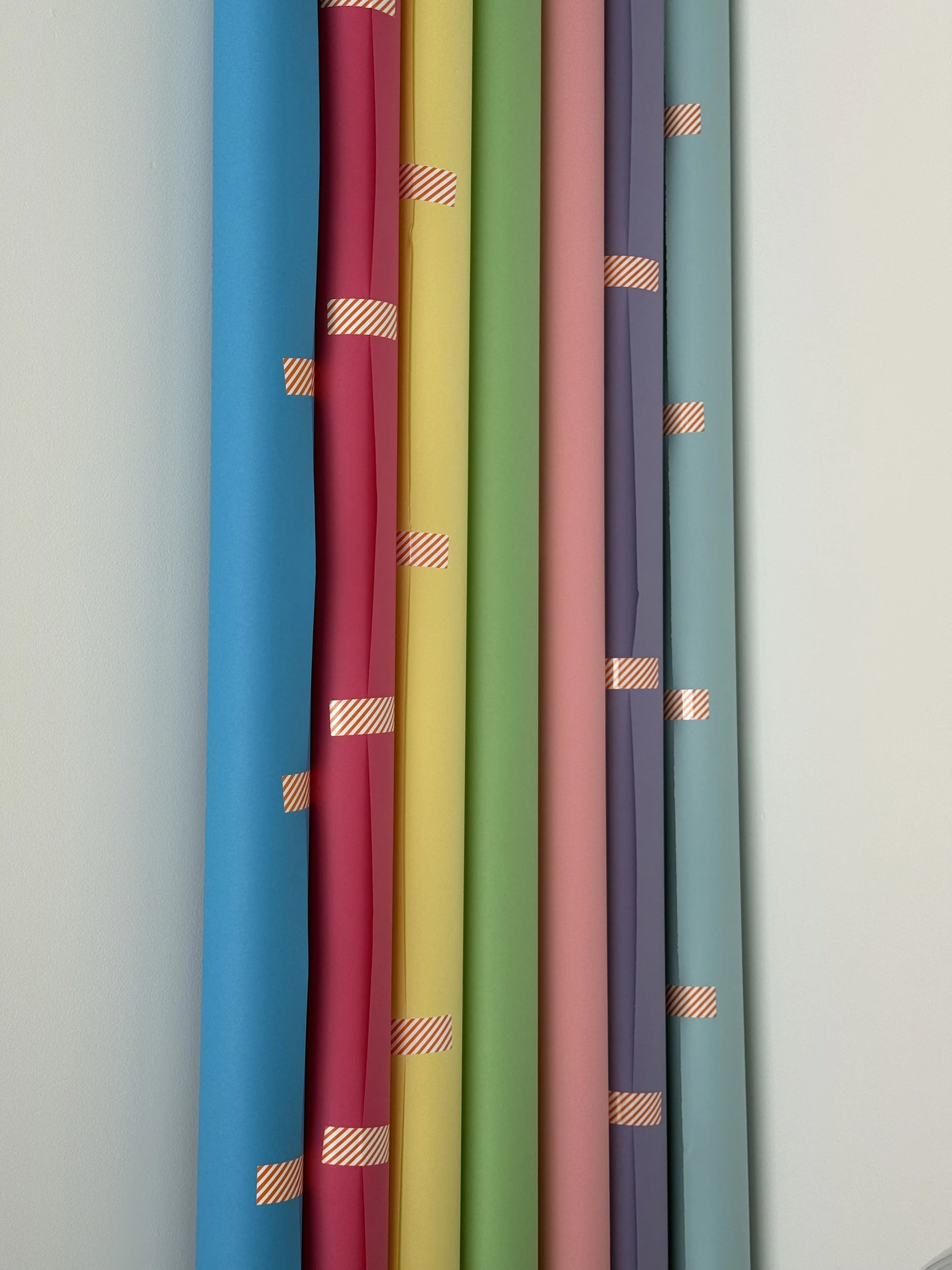 Colorful rolls of wrapping paper hung in a row on a wall.