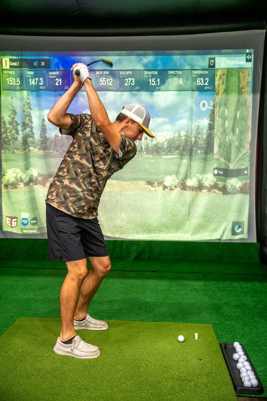 Man playing golf on Par-Tee Time's mobile golf simulator, swinging a golf club on a mat with golf balls on a tray.