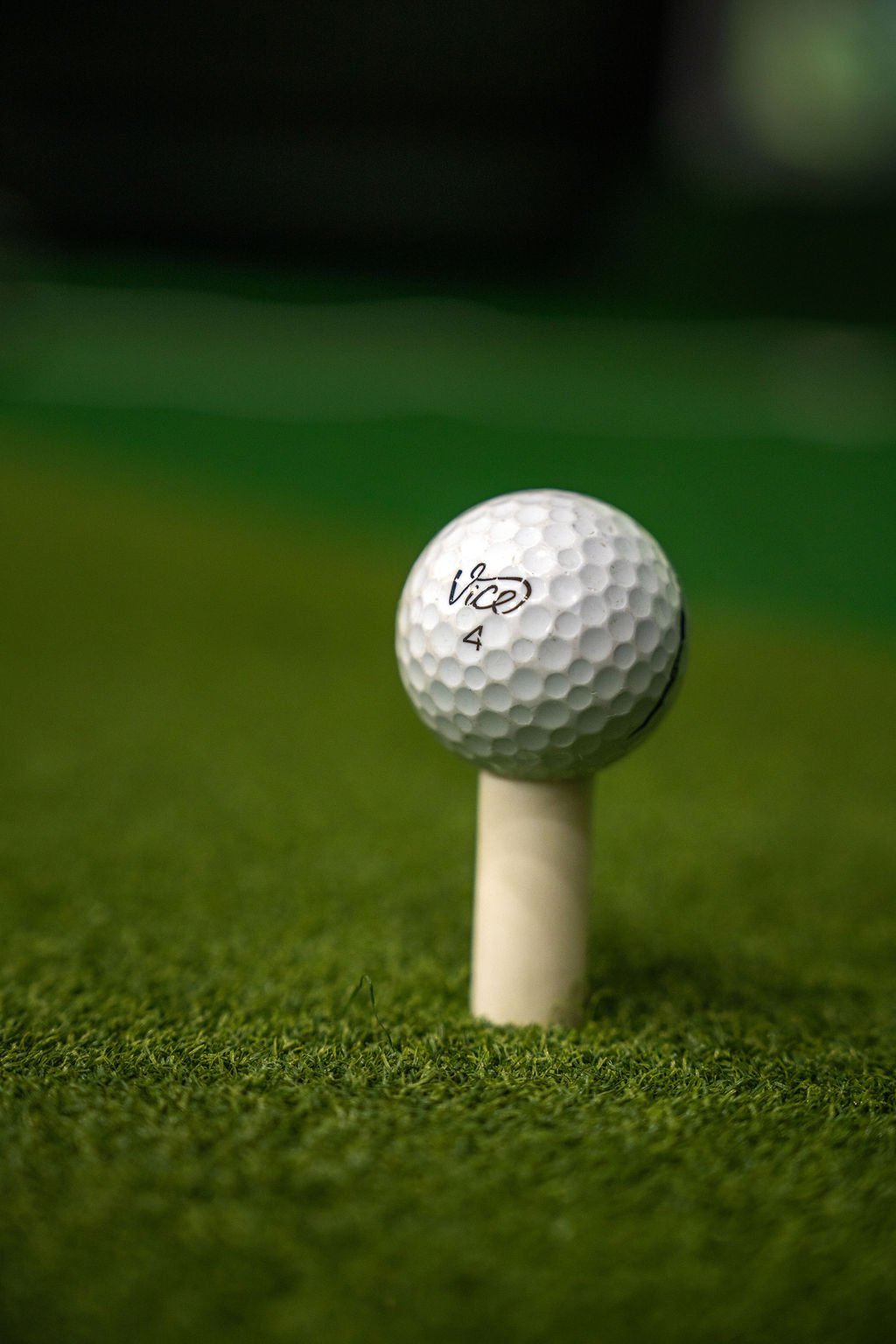 A close-up of a golf ball with the brand name 'Vice' sitting on a tee on green turf.