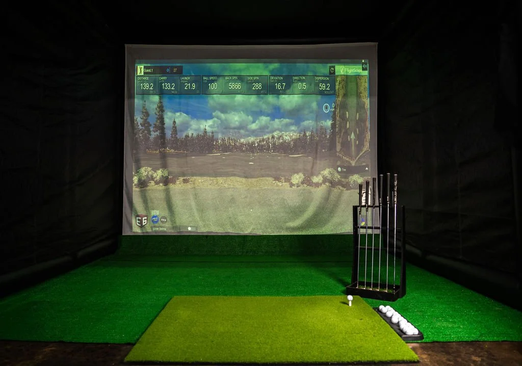 Par-Tee Time's mobile golf simulator with a screen displaying a golf course, golf clubs in a stand, and golf balls on the floor.