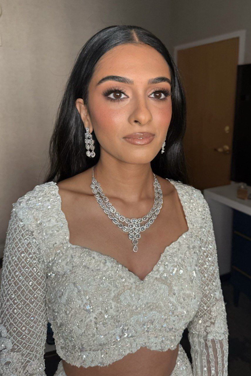 Woman dressed in a glittering white outfit with diamond jewelry, including earrings, necklace, and bracelet, posing indoors.