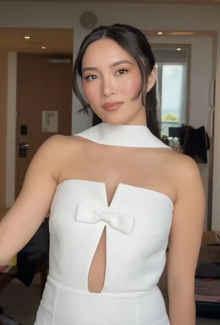 A woman in a stylish white dress with a bow and keyhole design, posing indoors with a confident expression.