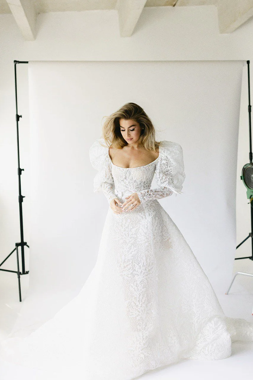 A woman in a white wedding dress standing in a photography studio with a white backdrop.