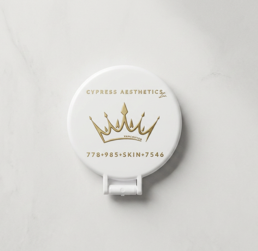 A white compact mirror with gold lettering and a crown logo, featuring the text 'Cypress Aesthetics Ltd.', 'Vancouver', and a placeholder phone number and skin code.